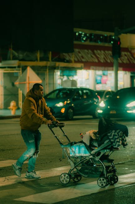 Busy dad ties running shoes beside a stroller on a city sidewalk before sunrise.